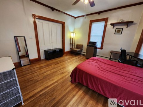 A bedroom with a red bedspread and wooden floors.
