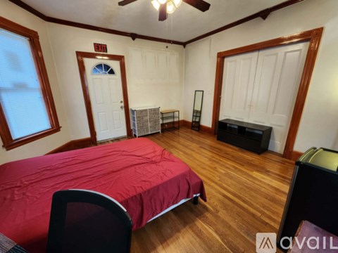 A bedroom with a red bedspread and a ceiling fan.