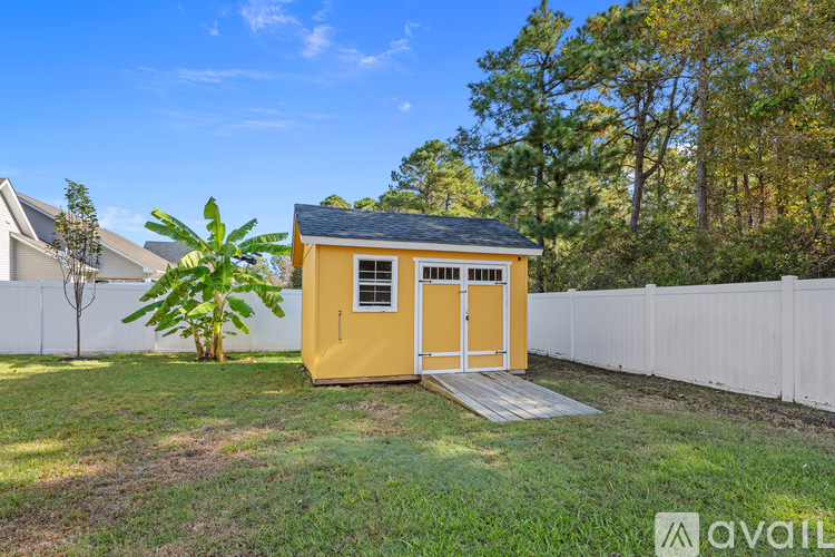 A yellow shed with a black roof is situated in a grassy area with a white fence and trees in the background.