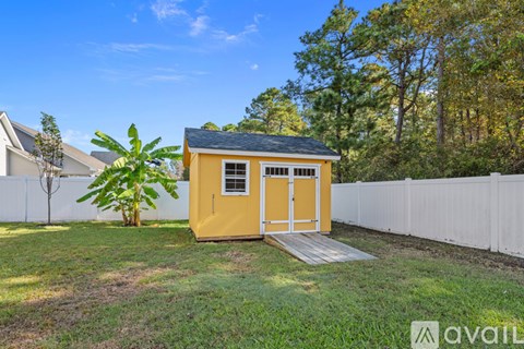 A yellow shed with a black roof is situated in a grassy area with a white fence and trees in the background.