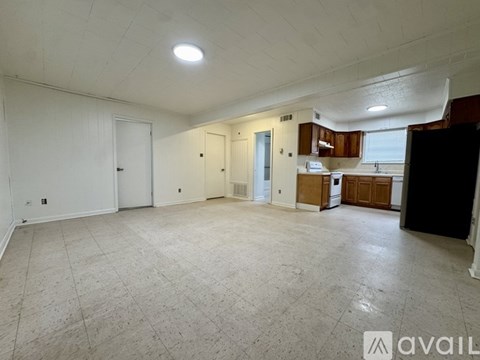 A spacious empty room with a kitchen area in the background.