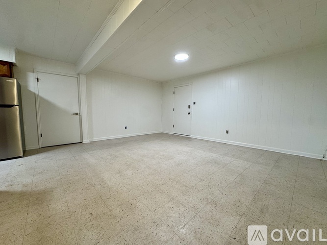 A spacious empty room with a refrigerator on the left side.