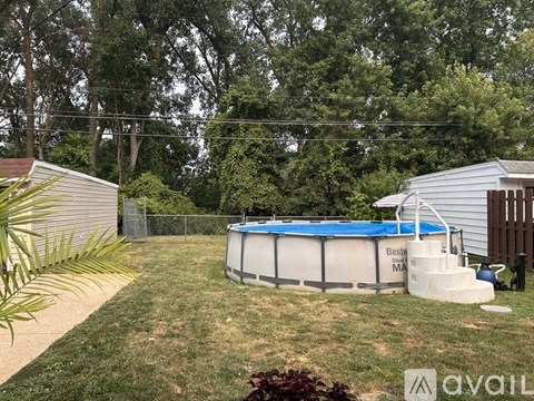 A pool with a blue cover and a white fence is surrounded by greenery.