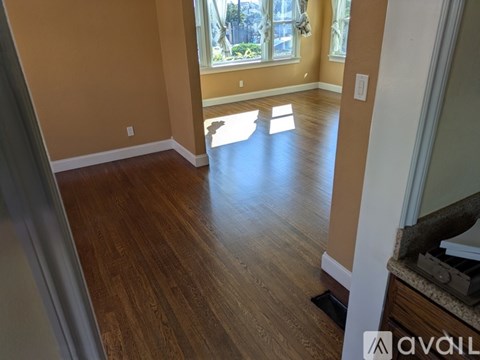 A room with wooden flooring and a window letting in sunlight.