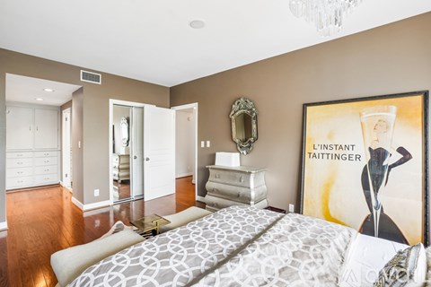 A bedroom with a large bed and a painting of a woman holding a glass.