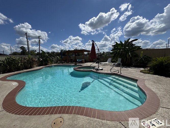 A small pool with a red umbrella and a white chair.