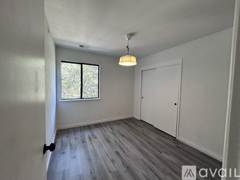 A room with a wooden floor, white walls, a window, and a door.