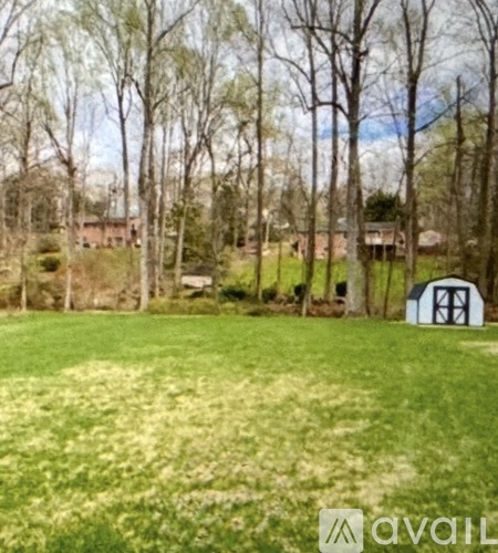 A grassy field with trees and a shed in the background.