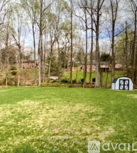 A grassy field with trees and a shed in the background.