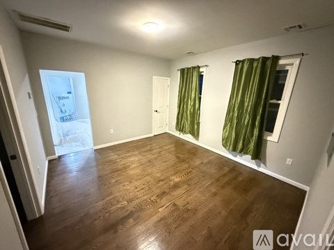 A room with wooden flooring and a window with green curtains.