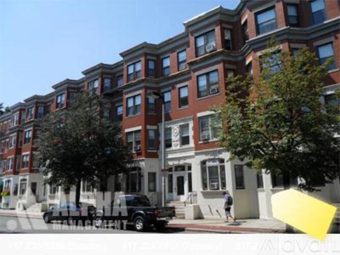 A street view of a row of brown and white buildings with a black car parked on the sidewalk.