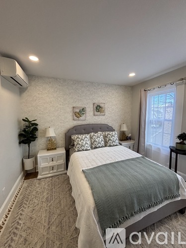 A bedroom with a bed, nightstand, and a plant.
