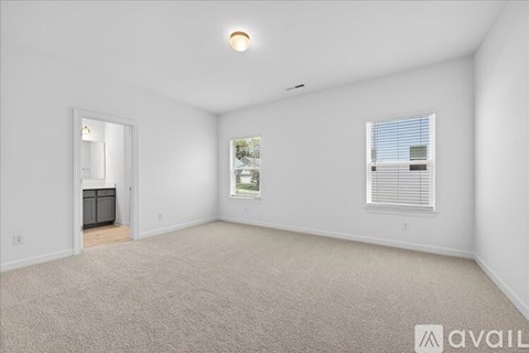 A spacious room with a carpeted floor, a window with blinds, and a door leading to another room.