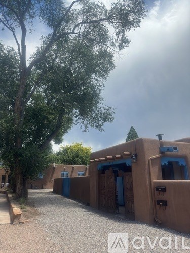 A series of adobe buildings with blue doors and windows are surrounded by trees.