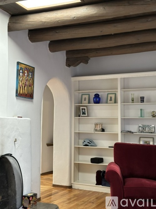 A living room with a red chair and a white shelf with various objects on it.