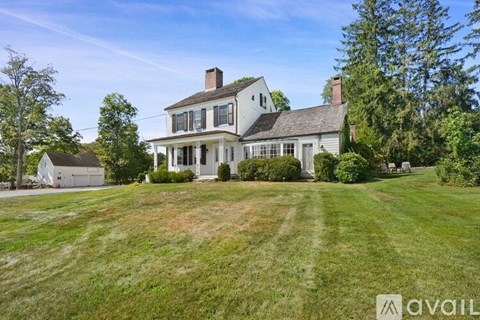 A large white house with a grey roof and a chimney is surrounded by a green lawn and trees.