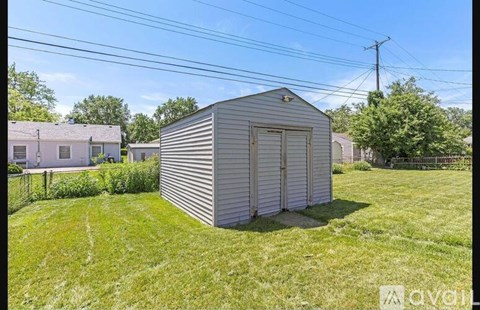 A shed sits in a grassy yard next to a house.