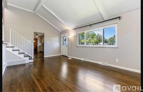 A spacious room with wood flooring and a staircase to the left.