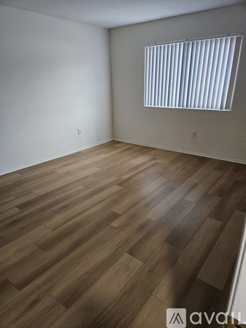 A room with wooden flooring and a window with blinds.