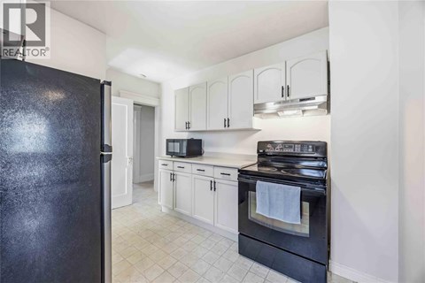 A black refrigerator is in a kitchen with white cabinets and a black stove.