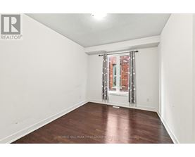 A room with a wooden floor and a window with a view of a brick building.