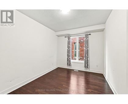 A room with a wooden floor and a window with a view of a brick building.