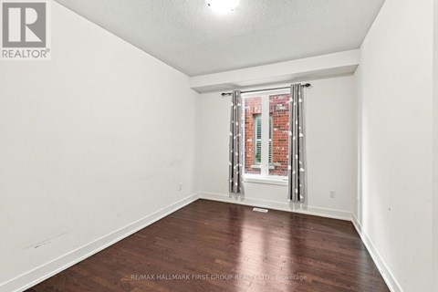 A room with a wooden floor and a window with a view of a brick building.