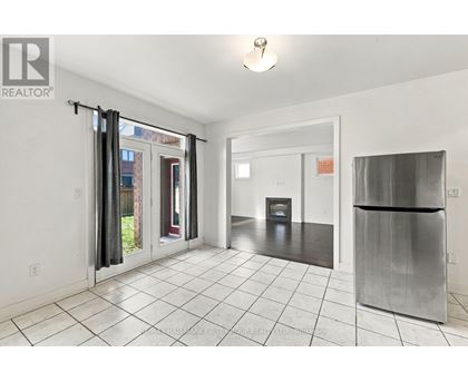 A white tiled kitchen with a refrigerator and a door leading outside.