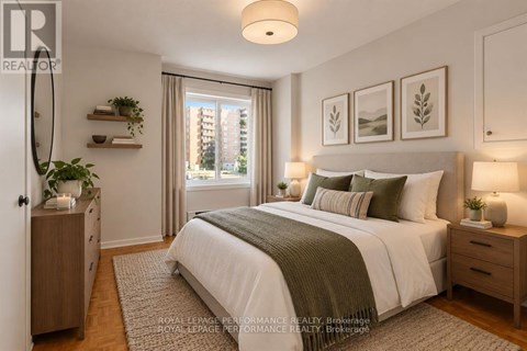 A bedroom with a large bed, a nightstand with a lamp, and a window with a view of a building outside.