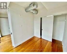 A room with wooden floors and white walls, with a door on the right and a window on the left.