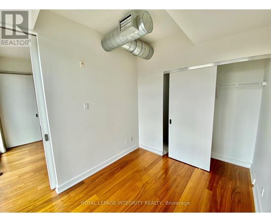 A room with wooden floors and white walls, with a door on the right and a window on the left.