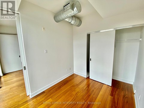 A room with wooden floors and white walls, with a door on the right and a window on the left.