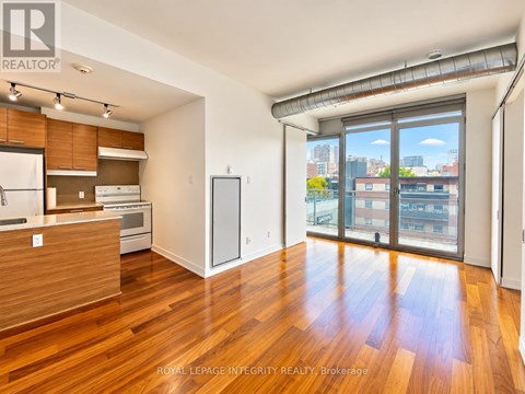 A spacious room with wooden floors and a kitchen area with a refrigerator, oven, and microwave.