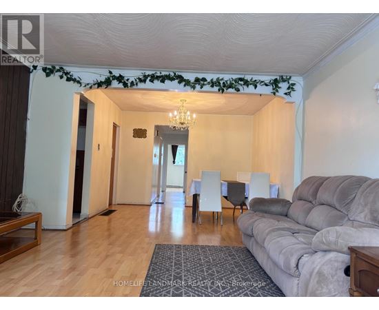 A living room with a grey couch, a dining table with chairs, and a chandelier.