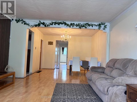 A living room with a grey couch, a dining table with chairs, and a chandelier.