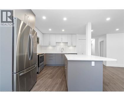 A modern kitchen with a stainless steel refrigerator and wooden flooring.