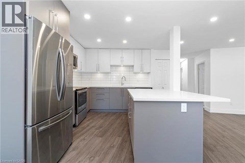 A modern kitchen with a stainless steel refrigerator and wooden flooring.