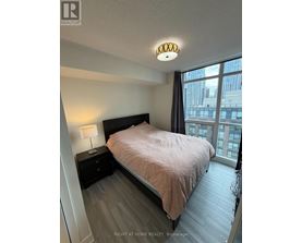 A bedroom with a bed, nightstand, and window overlooking a cityscape.