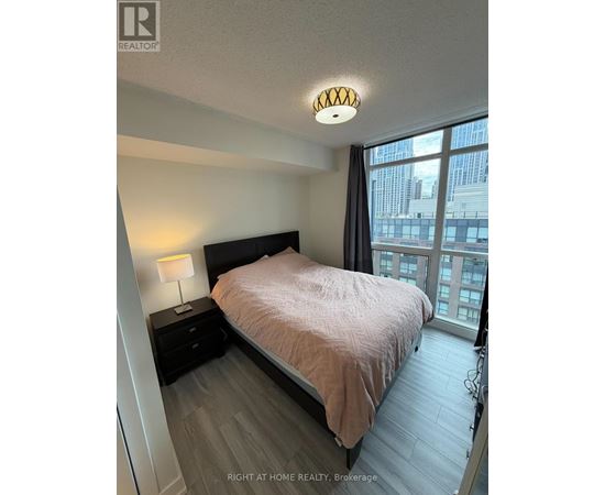 A bedroom with a bed, nightstand, and window overlooking a cityscape.