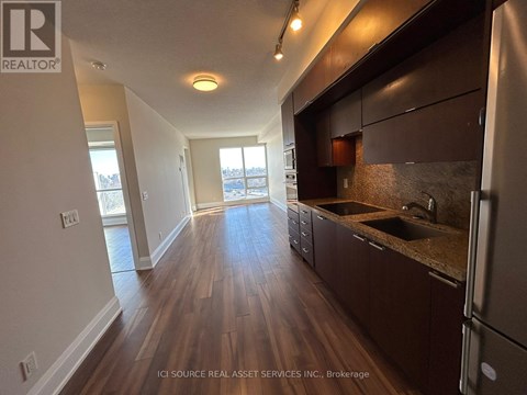A kitchen with dark wood floors and a refrigerator on the right.