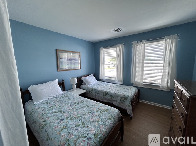 A bedroom with two beds and a window with white curtains.