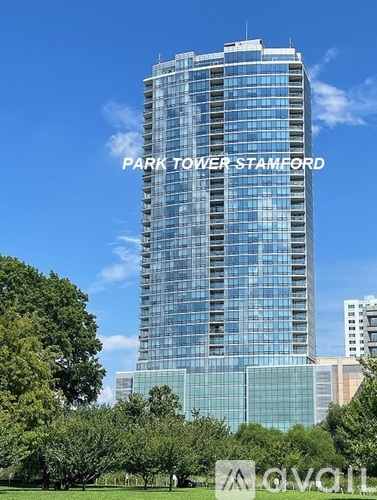 A tall glass building named Park Tower Stamford stands in front of a blue sky.