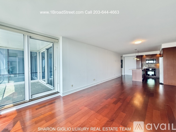 A real estate listing image featuring a spacious room with wood flooring and a glass door leading outside.