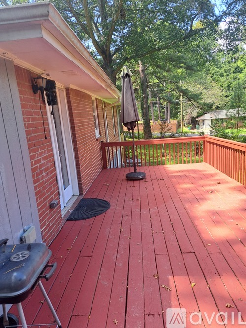 A red wooden deck with a grill and an umbrella.