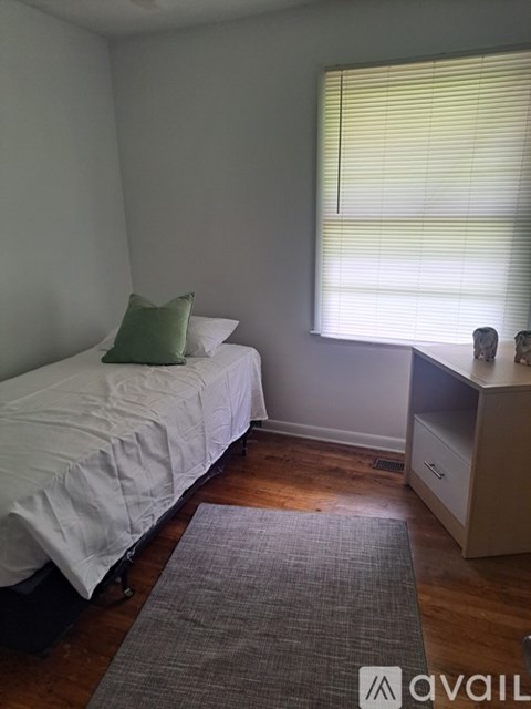 A bedroom with a bed, a window with blinds, a nightstand, and a rug.