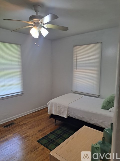 A room with a bed, a table, and a ceiling fan.