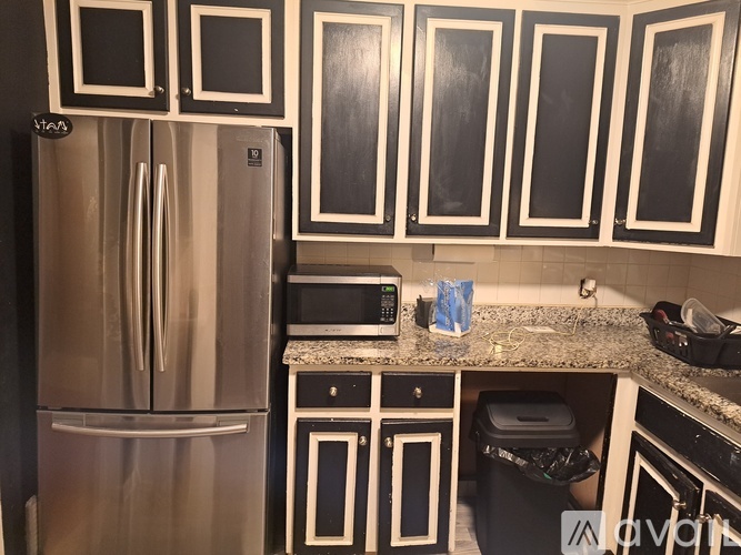 A kitchen with a stainless steel refrigerator and black and white cabinets.