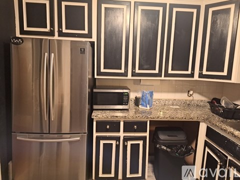 A kitchen with a stainless steel refrigerator and black and white cabinets.