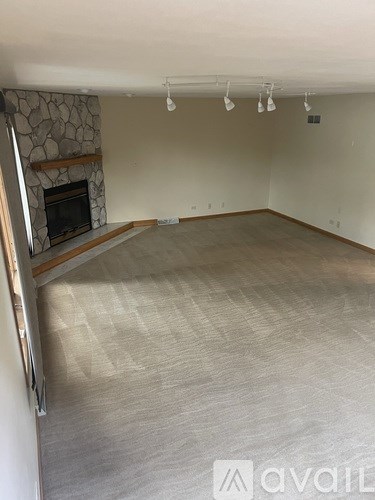 A living room with a stone fireplace and a carpeted floor.
