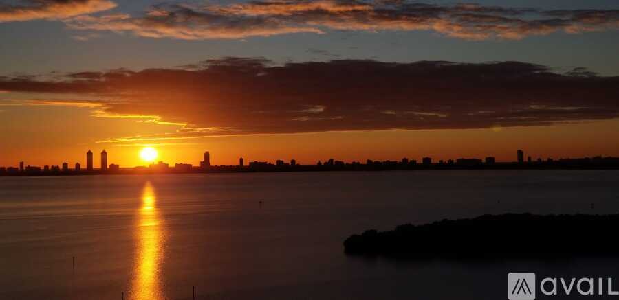 The sun is setting over a city skyline with a reflection on the water.